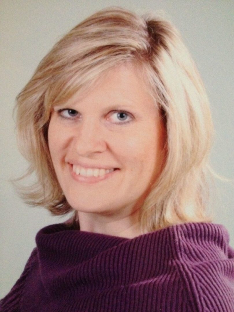 A woman with blonde hair wearing a purple sweater.
